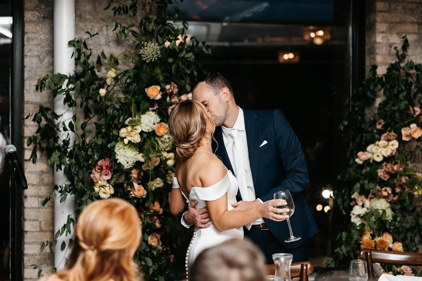 A bride and groom share a romantic kiss during their intimate elopement ceremony, surrounded by friends and family.